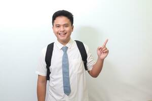 Indonesian senior high school student wearing white shirt uniform with gray tie showing product, pointing at something and smiling. Isolated image on white background photo