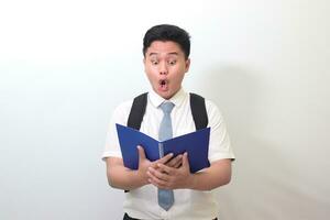 Indonesian senior high school student wearing white shirt uniform with gray tie shocked and looking at his note book. Isolated image on white background photo