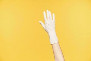 Close-up of raised hand in white rubber glove posing over orange background, keeping all fingers separately. Preparing for spring cleaning of house photo