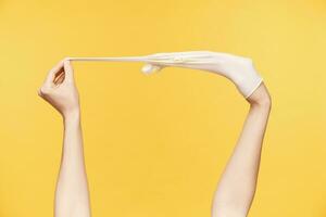 Cropped shot of young female's hands being raised white taking out rubber gloves, posing over orange background. Cleaning and human hands concept photo