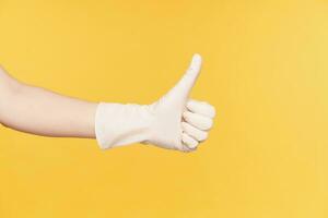 Horizontal photo of raised hand in white gloves showing thumb while demonstrating well done sign, isolated over orange background. Body language and gesturing concept