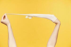 Indoor shot of young female's raised hands being isolated over orange background while pulling out white rubber glove. Being glad to finish spring cleaning of house photo