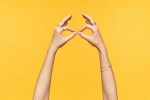 Side view of fair-skinned hands of young female being isolated over yellow background while imitating with folded fingers eyeglasses. Hands and body language concept photo