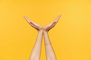 Cropped photo of young fair-skinned woman raising her palms up and folding them in semicircle while standing over yellow background. Body language and signs concept