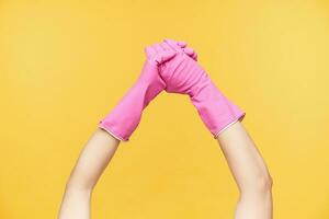 Cropped young woman's hands in pink gloves being crossed while washing hands with soap, isolated over orange background. Human hands and cleaning concept photo