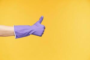 Side view of raised hand showing thumb up while expressing positive emotions, forming like gesture with raised finger while posing over yellow background photo