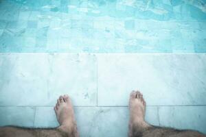 Relaxing man with his feet on poolside at swimming pool photo