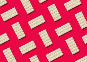 Trendy pattern made of white chocolate on red background. Minimal concept. Yummy sweet food idea. Creative chocolate bars composition. White chocolate aesthetic background. Flat lay. photo