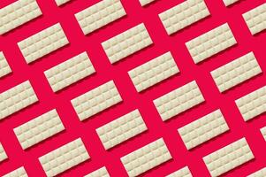 Trendy pattern made of white chocolate on red background. Minimal concept. Yummy sweet food idea. Creative chocolate bars composition. White chocolate aesthetic background. Flat lay. photo