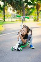 Cute little asian girl learning to ride a scooter in a park photo