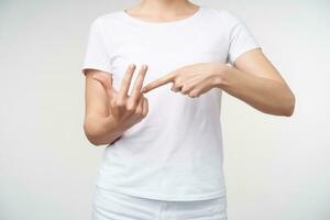 Indoor shot of young female dressed in casual clothes raising hands while talking on sign language, showing word counting while posing over white background photo