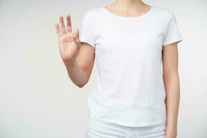 Studio shot of young woman showing raised hand while forming with fingers number nine using sing language, isolated aginst white background in casual wear photo