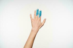 Studio photo of elegant woman's raised hand with blue paint on forefinger and middle finger pulling it ahead while being isolated over white background