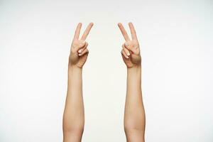 Studio photo of two raised female hands with white manicure showing peace gesture while posing over white background. Informal ladies hand emotions