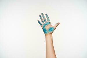 Cropped photo of fair-skinned pretty woman's hand showing raised palm with blue paint on it, standing over white background. Human hands and signs concept