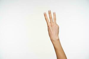 Cropped shot of woman's hand with white manicure keeping three fingers raised while showing counting gesturing, being isolated over white background photo