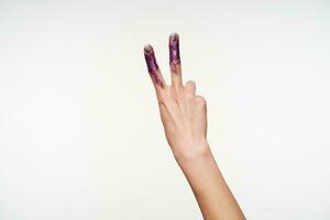 Front view of painted woman's hand being raised while forming victory gesture with raised two fingers, being isolated over white background. Hand gesturing concept photo