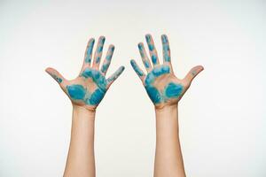 Studio photo of fair-skinned female's hands with blue paint on it showing palms and keeping all fingers separately, being isolated over white background