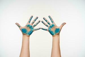 Horizontal photo of raised female's arms painted with blue colour keeping all fingers separately while posing over white background. Body language concept