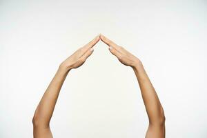 Raised female's pretty arms imitating house with folded palms while standing over white background, language hand symbol viewed from side view photo