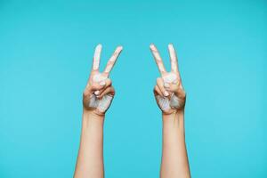 Studio shot of lady's stained hands being raised while showing letter V in sign language hand symbol viewed from back, isolated over blue background photo