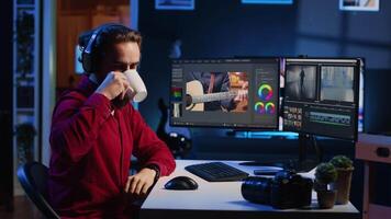 Videographer using editing software to assemble footage into cohesive final result while enjoying cup of coffee. Specialist color correcting clips while listening music in headphones video