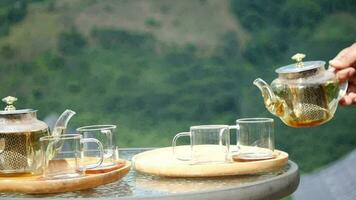 A hand pouring tea from glass teapot on wooden serving tray, hands pouring tea from teapot, Cropped shot of pouring tea in traditional chinese teaware video