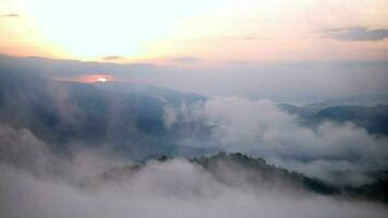 The mist flows through the mountain forest, Sun shining into tropical forest, Mist drifts through mountain ridges in the morning, slow floating fog blowing cover on the top of mountain video