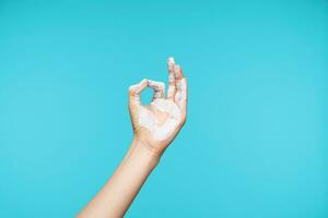 Photo of painted in white color hand being raised while showing mudra gesture, posing over blue background while meditating. Body language concept