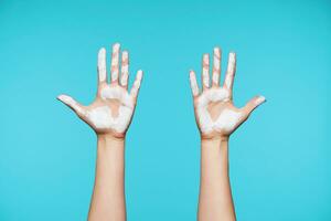 Two female's fair-skinned arms showing up raised palms with white paint while posing over white backgound. Human hands and gesturing concept photo