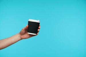 Photo of black paper cur with coffee being held by young female with white manicure, suggesting hot drink to her friend while standing over blue background