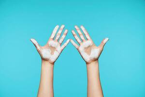 Two young female's hands showing up palms with white paint on it and keeping all fingers separately, isolated against blue background. Human gestures concept photo