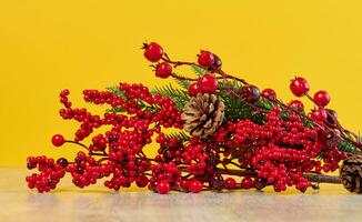 decorativo Navidad rama con rojo bayas y pino conos en un amarillo antecedentes foto