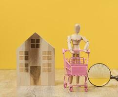 Wooden house and miniature figurines on a yellow background. The concept of selling and buying real estate, investment photo