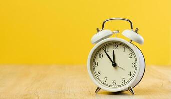 Round white alarm clock, the time is five minutes to twelve. Yellow background photo