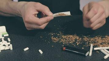 Man in Black Clothing is Rolling a Hand Made Cigarette Using Papers, Filters and Tobacco. A Way to Save on Tobacco Products. Tobacco Product Economy Concept. CloseUp Shot video