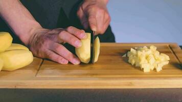 chef dans noir uniforme est trancher brut pomme de terre. homme dans une cuisine est Coupe Patate et en train de préparer Ingrédients pour cuisine lent mouvement. statique coup video