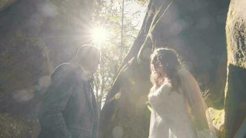 Hochzeit Paar Wer sind zwischen das Felsen auf ein sonnig Tag. ein Mann nähert sich ein Frau, das Sonne Strahlen leuchtenden in das Kamera mit ein Hintergrundbeleuchtung. Blendung von Licht ist reflektiert im das Kamera. video