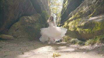 The bride in a wedding dress runs and smiles at the camera. The sun's rays of backlight illuminate the camera with flashes. The bride runs between the rocks video