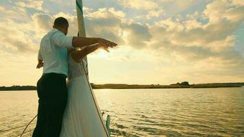 Newlyweds stand on a bow of a sailing yacht like in Titani. Newlyweds on a background of beautiful sunset video