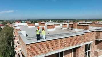 bouw van een huis. twee bouw architecten inspecteren de bouw plaats Aan de dak van een hoogbouw gebouw. video