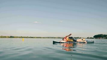 een Mens zwemmen aan het liegen naar beneden Aan een sup bord en roeien met een hand. de lucht en de bovenste voor de helft van de kader net zo een plaats voor tekst. video