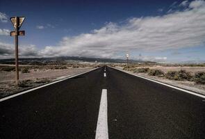un vacío la carretera con un oxidado firmar en medio de Desierto foto
