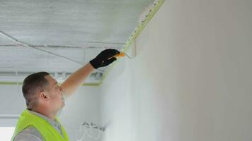 A Caucasian man is painting a wall to refresh it and cover stains. Using a roller in hand, a painter paints a textured wall in a white color using white color paint. Renovation concept. video