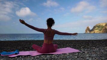 Jeune femme avec noir cheveux, aptitude instructeur dans leggings et hauts Faire élongation et pilates sur yoga tapis près le mer. femelle aptitude yoga routine concept en bonne santé mode de vie harmonie et méditation video