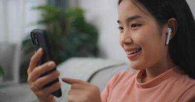 Portrait young asian woman relax on comfortable couch at home shopping online on smartphone, smiling girl use cell phone chatting, browse wireless internet on gadget photo