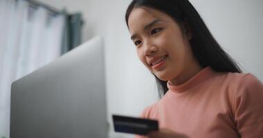 Portrait of Young asian woman sitting on sofa in living room, makes online banking payments through the internet from bank card on laptop,Shopping online with credit card. photo