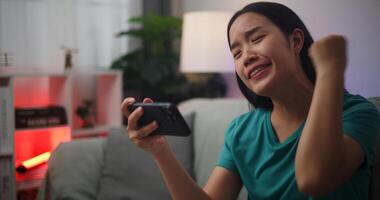 Portrait of Young Asian woman enjoys playing online esport games on smartphone sitting on sofa in the living room at home,Gamer lifestyle concept,Gamer lifestyle concept. photo