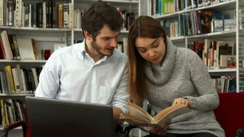 Studenten vergleichen Sie Information im das Buch und auf das Laptop beim das Bibliothek video