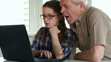 Senior man and his granddaughter watch something on laptop video